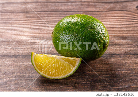 Fresh whole lime and a cut juicy wedge on a rustic dark wood background Fresh whole lime and a cut juicy wedge on a rustic dark wood background 138142616