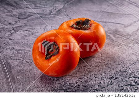 Two fresh ripe orange persimmons on a grey textured surface Two fresh ripe orange persimmons on a grey textured surface 138142618