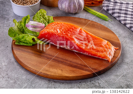 Fresh raw salmon fillet with lettuce, onion, and garlic on a wooden cutting board. Fresh raw salmon fillet with lettuce, onion, and garlic on a wooden cutting board. 138142622