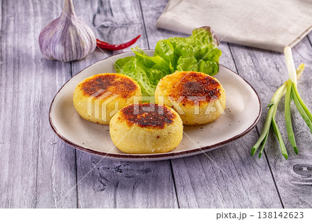 Golden fried potato patties served with fresh lettuce, garlic, and spring onions on a rustic wooden table. 138142623