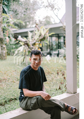 Portrait of Asian Man Sitting Relaxed Outdoors Looking at Camera 138142746