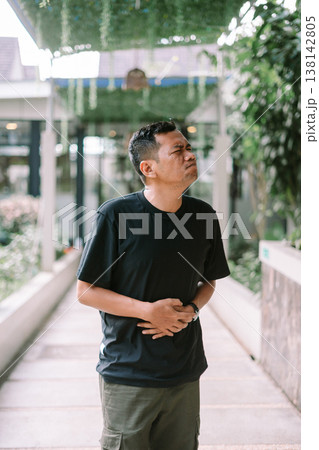 Man holding stomach in pain showing abdominal discomfort in outdoor setting 138142805