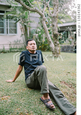 Relaxed Asian Man Sitting on Grass Leaning Back Enjoying Nature Relaxed Asian Man Sitting on Grass Leaning Back Enjoying Nature 138143362