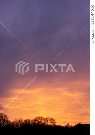 Dramatic sunset over forest with vibrant purple and orange clouds in the sky 138144010