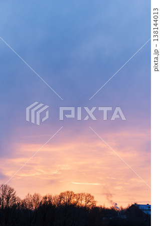 Dramatic pastel sunset sky above dark winter trees and distant buildings Dramatic pastel sunset sky above dark winter trees and distant buildings 138144013