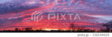 Epic panoramic fiery sunset sky with textured clouds and tree silhouettes Epic panoramic fiery sunset sky with textured clouds and tree silhouettes 138144020
