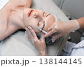Woman head lying with closed eyes while a dermatologist or aesthetician in gloves performs a facial injection near the eye area in a wellness clinic, close-up. 138144145