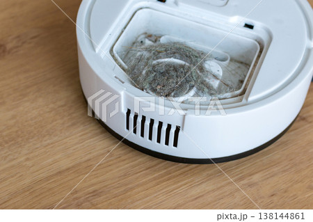White robot vacuum cleaner with full dustbin container on wooden floor, maintenance and domestic housework concept. White robot vacuum cleaner with full dustbin container on wooden floor, maintenance and domestic housework concept. 138144861