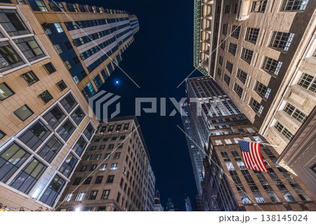 Skyscrapers viewed from street level with American flag in Manhattan at night Skyscrapers viewed from street level with American flag in Manhattan at night 138145024
