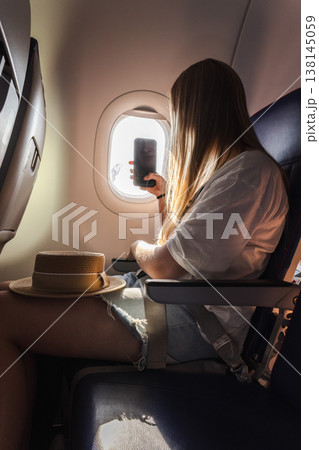 Young woman photographing view through airplane window during flight Young woman photographing view through airplane window during flight 138145059