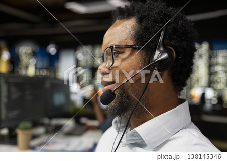 Close up of startup helpdesk admin speaking in headset microphone, responding to service alerts. African american IT expert in office doing tech support, helping users across remote infrastructure 138145346