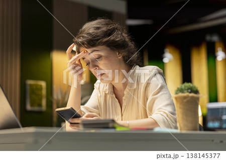 Confused employee checking her calendar before scheduling an engagement, picking up her mobile phone to answer texts and read notifications. Woman getting distracted and frowning. 138145377