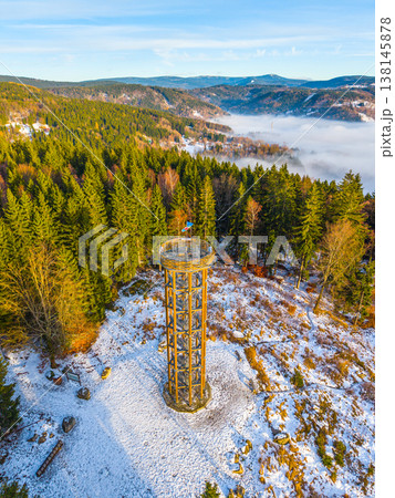 Svetly vrch lookout tower stands tall in Albrechtice, surrounded by snow-covered trees and mountains. This scene captures the winter landscape with a clear blue sky and distant hills. 138145878