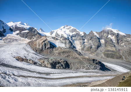 Piz Bernina rises majestically in the Swiss Alps, surrounded by rugged mountains and sprawling glaciers. The clear blue sky enhances the breathtaking landscape in Graubunden, Switzerland. 138145911