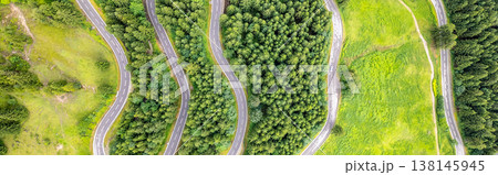 Curving asphalt roads meander through dense forests in the Alps, offering breathtaking aerial views during a scenic mountainous road trip in summer. Nature surrounds the serpentine path. 138145945