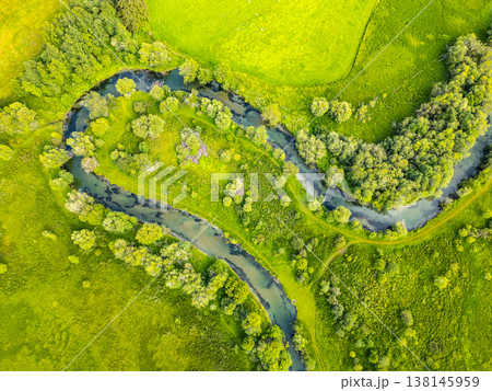 A serene river gracefully winds through a vibrant green valley in the Alps. Lush vegetation surrounds the creek, creating a picturesque landscape from a drone's perspective. A serene river gracefully winds through a vibrant green valley in the Alps. Lush vegetation surrounds the creek, creating a picturesque landscape from a drone's perspective. 138145959