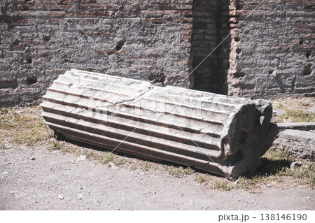 An ancient column lies on the ground among the remains of a structure. The column shows signs of wear with detailed grooves and is part of a historic site. 138146190