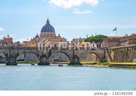 St Peters Basilica stands tall in the background as people enjoy leisure activities on the Tiber River. The bridge connects both sides while boats move gently along the water. St Peters Basilica stands tall in the background as people enjoy leisure activities on the Tiber River. The bridge connects both sides while boats move gently along the water. 138146208