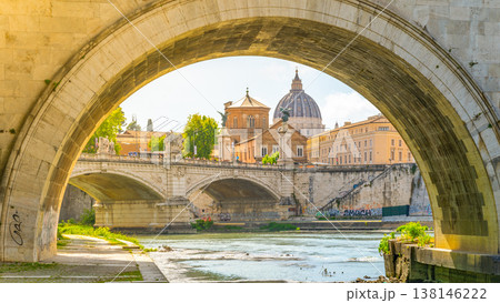 A scene of St. Peters Basilica seen from under the bridge over the Tiber River. The sun shines on the water and buildings, capturing a moment in Rome's city life. A scene of St. Peters Basilica seen from under the bridge over the Tiber River. The sun shines on the water and buildings, capturing a moment in Rome's city life. 138146222
