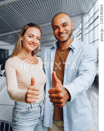 Couple shows thumbs up gesture inside car dealership during the day 138146864