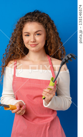 Woman holds garden tools against a blue background in a sunny setting Woman holds garden tools against a blue background in a sunny setting 138146874