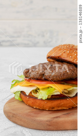 Juicy burger with layers of vegetables and cheese served on a wooden board Juicy burger with layers of vegetables and cheese served on a wooden board 138146889