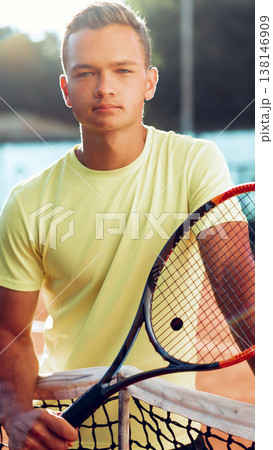 Young tennis player poses with racket on court in bright sunlight during afternoon practice session Young tennis player poses with racket on court in bright sunlight during afternoon practice session 138146909
