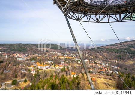 The scene shows a view from a high observation deck. Trees and hills surround a small town with colorful buildings. A clear sky can be seen in the background. The scene shows a view from a high observation deck. Trees and hills surround a small town with colorful buildings. A clear sky can be seen in the background. 138146941