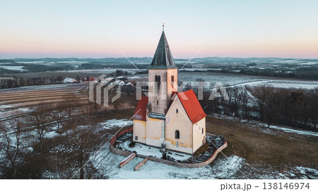 Aerial view shows the Church of St. James in Chvojen. The surroundings include fields and trees with snow. The image captures the structure's shape and the landscape during winter. 138146974