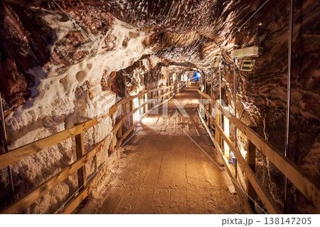 A wooden pathway stretches through a salt mine tunnel, illuminated by soft lights, showcasing intricate rock formations. This underground world creates a unique and immersive experience. A wooden pathway stretches through a salt mine tunnel, illuminated by soft lights, showcasing intricate rock formations. This underground world creates a unique and immersive experience. 138147205