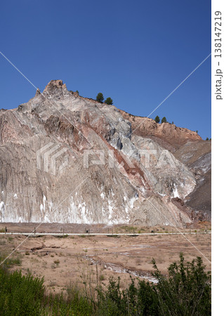 A scenic view showcases layered rock formations under a vibrant blue sky, displaying natural beauty. The landscape features earth-toned hues and distant trees. A scenic view showcases layered rock formations under a vibrant blue sky, displaying natural beauty. The landscape features earth-toned hues and distant trees. 138147219