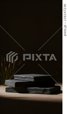 Three natural slate stone pedestals in a minimalist dark setting with dry grass, ideal for product display. 138147236