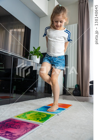 Little girl stepping and jumping on colorful sensory gel mats placed on floor at home. Sensory development, autism support and occupational therapy activity concept. 138148645
