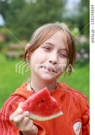 A girl in nature eats a red watermelon and smiles. Happy girl eating watermelon in nature 138148684