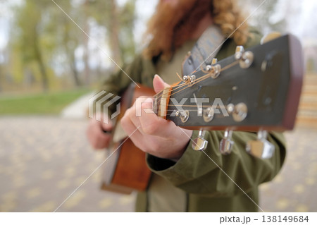 Close-up of the guitar neck, focus on the hand of a man pinching a chord. A guy with long red hair plays the guitar. The guitarist is wearing a green jacket Close-up of the guitar neck, focus on the hand of a man pinching a chord. A guy with long red hair plays the guitar. The guitarist is wearing a green jacket 138149684