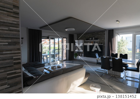 Modern modular house interior with smart home robot vacuum on sunset-lit open-plan living and dining area 138151452