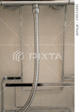 Shower hose connecting to a chrome fixture, forming part of a shower caddy and modern bathroom organization system against a tiled wall 138152885