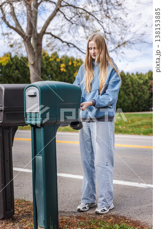 Young woman opening mailbox on suburban roadside in United States residential neighborhood Young woman opening mailbox on suburban roadside in United States residential neighborhood 138153885