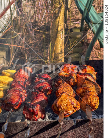 Skewered meat and potatoes grilling over charcoal outdoors 138154024
