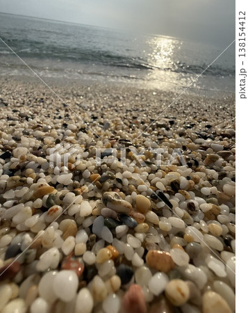 Pebble-covered beach shoreline with gentle waves and sunlight reflecting on water surface Pebble-covered beach shoreline with gentle waves and sunlight reflecting on water surface 138154412