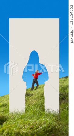 Woman walking through human silhouette paper cutout in grassy hill landscape. 138154552