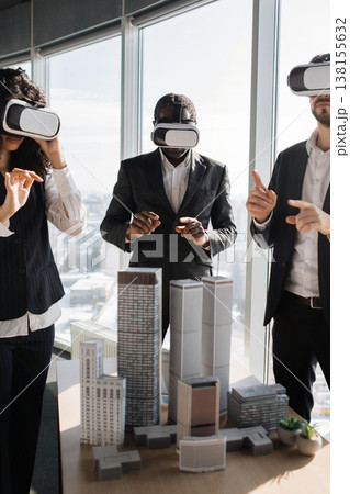 Three professionals in suits wearing VR headsets interact with a miniature city model during a virtual reality business meeting 138155632