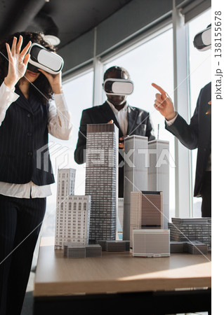 Colleagues in suits explore a virtual architectural scale model with VR headsets around a conference table to review design concepts and planning strategies for a new development project 138155678