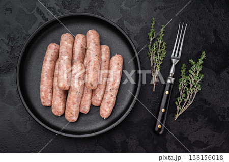 Uncooked pork sausage links made from minced meat served on black plate with thyme, rustic food composition 138156018