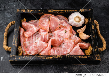 Assorted Milano salami slices in wooden tray with garlic cloves on dark textured background. 138156028