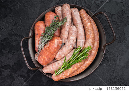 Raw sausage assortment in metal pan on dark kitchen background. Fresh pork meat links ready for grilling barbecue preparation. Raw sausage assortment in metal pan on dark kitchen background. Fresh pork meat links ready for grilling barbecue preparation. 138156031