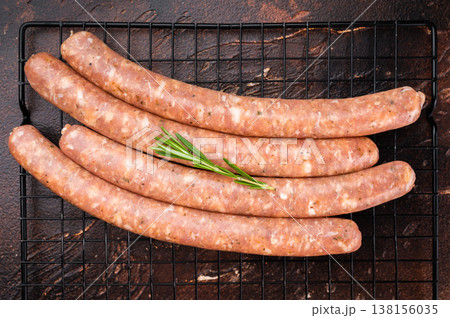 Raw fresh Chipolata sausages on metal grill rack with rosemary and coarse salt on dark rustic background. Uncooked pork meat links ready for grilling barbecue. Raw fresh Chipolata sausages on metal grill rack with rosemary and coarse salt on dark rustic background. Uncooked pork meat links ready for grilling barbecue. 138156035