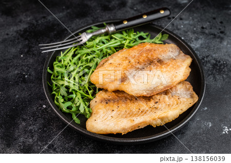 Pan seared tilapia fish fillets with arugula salad on plate over dark textured background, seafood meal. Pan seared tilapia fish fillets with arugula salad on plate over dark textured background, seafood meal. 138156039