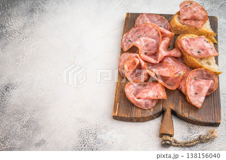 Top view salami slices with bread on rustic wooden board with peppercorns on light textured background. Top view salami slices with bread on rustic wooden board with peppercorns on light textured background. 138156040