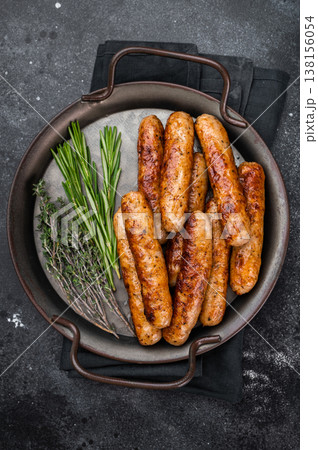 Fried sausage links with herbs in metal pan over dark textured background. Golden browned pork sausages freshly cooked for meal. 138156054